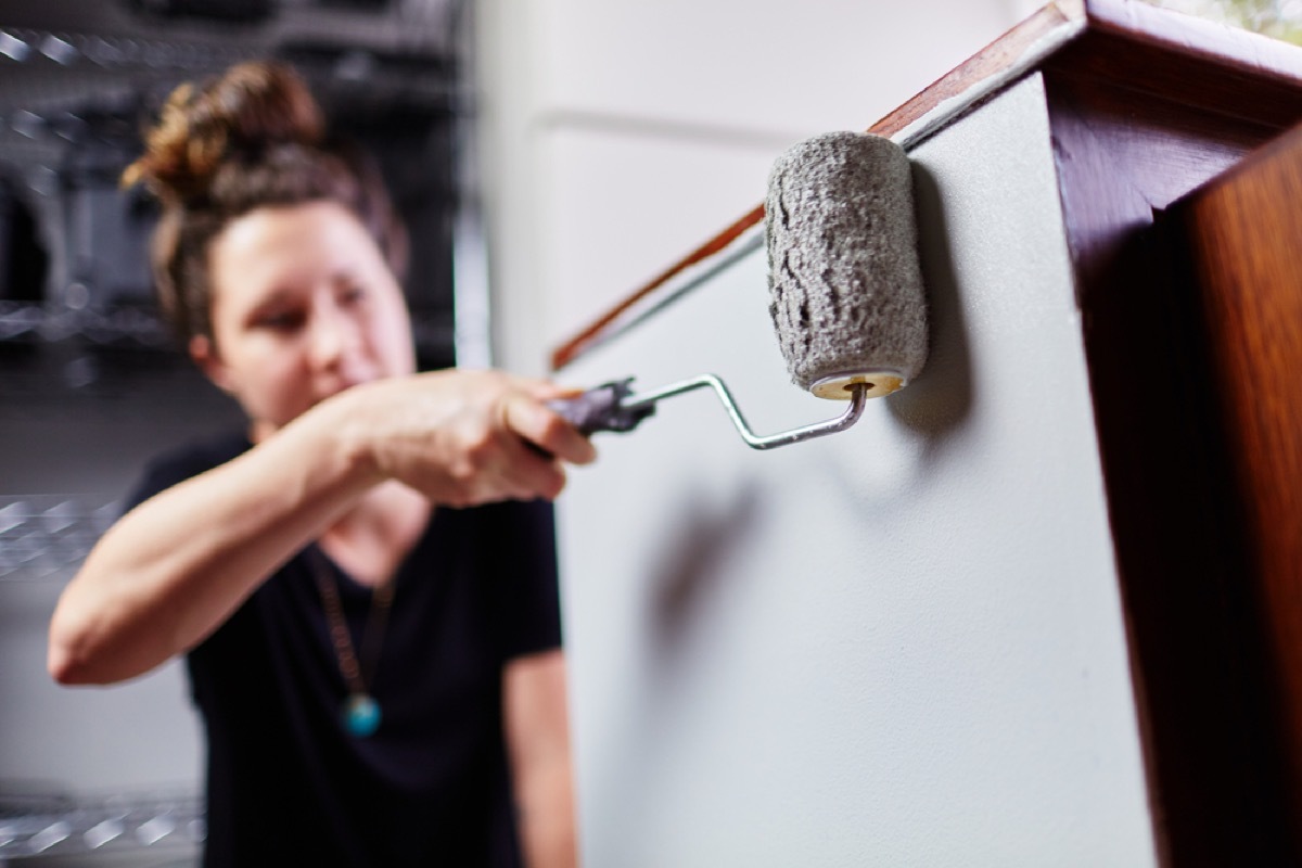 woman painting cabinets gray with a roller