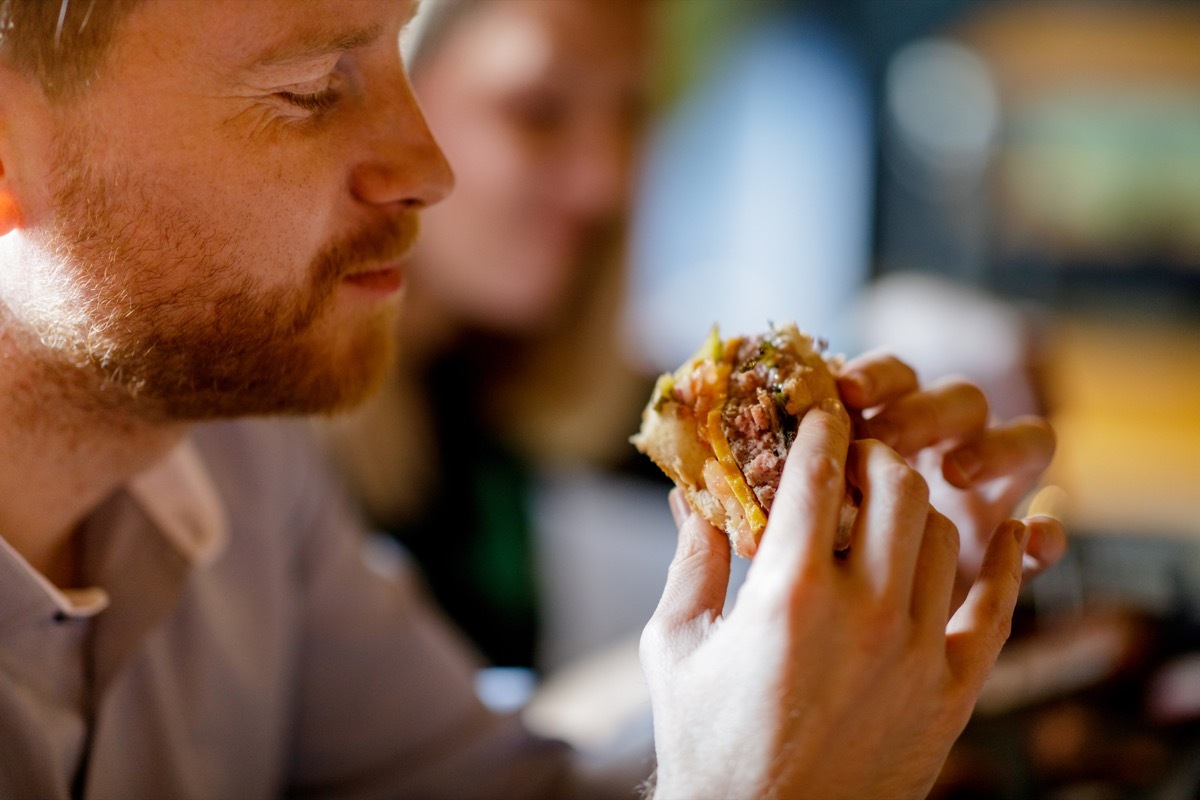 man holding a burger sandwich, sitting in a pub