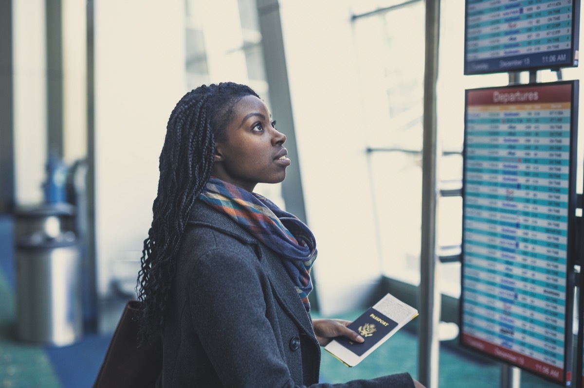 Young African American woman at airport holding passport and looking at the departures board