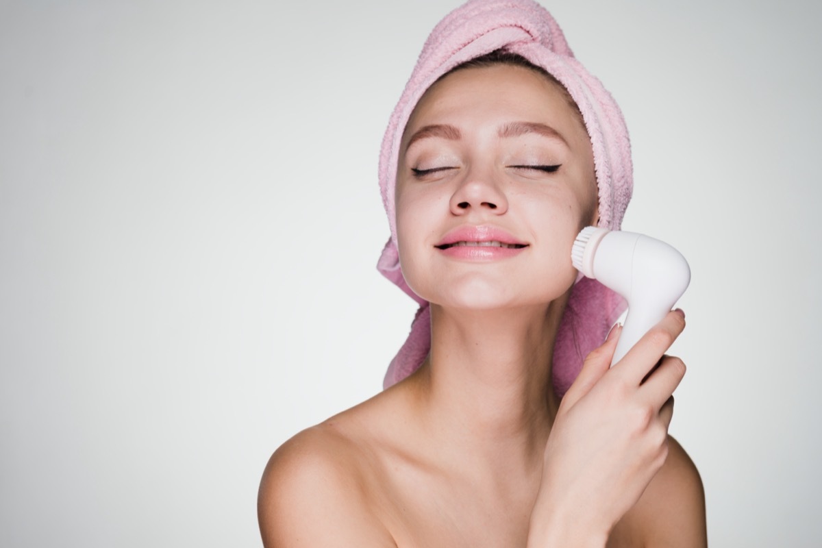 with a towel on her head doing face cleansing with a special electric brush