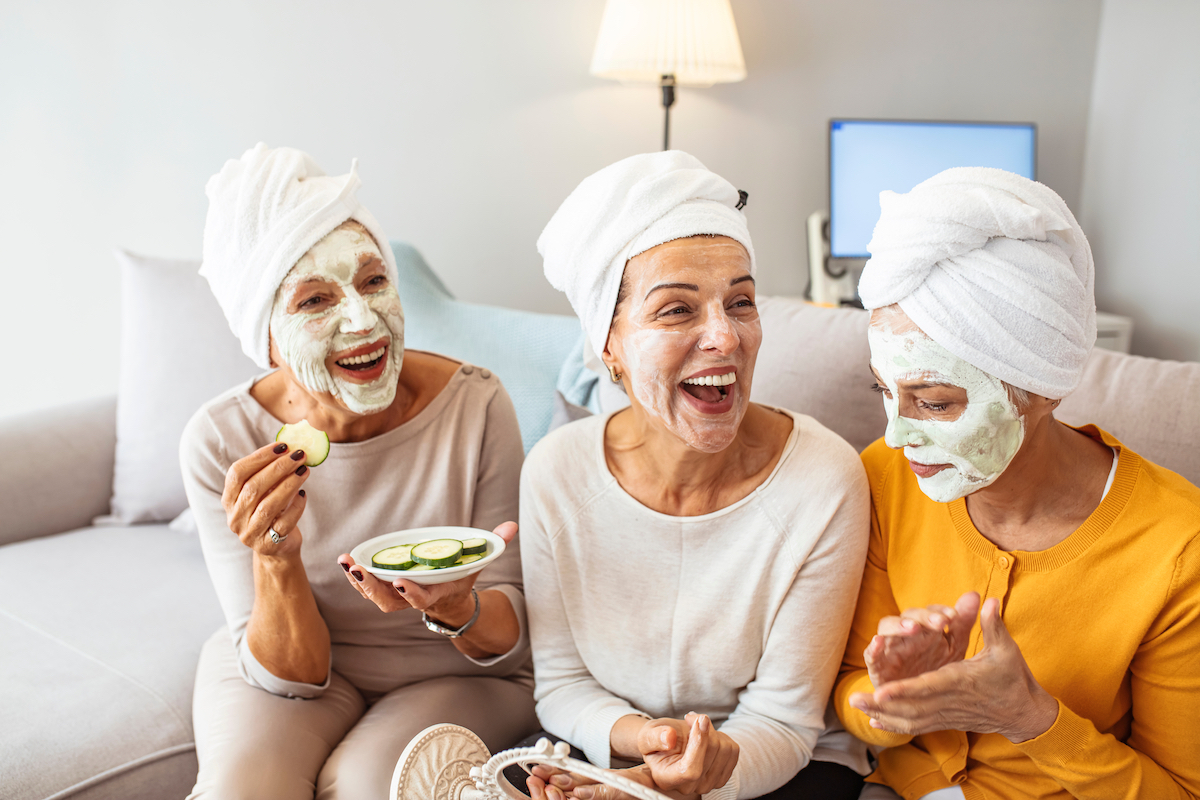 Three mature happy women with face masks at home.