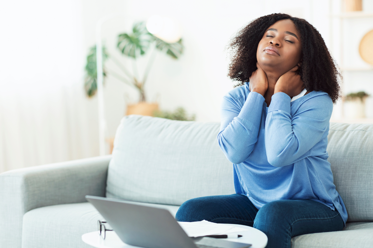 young woman sitting on couch massaging sore neck