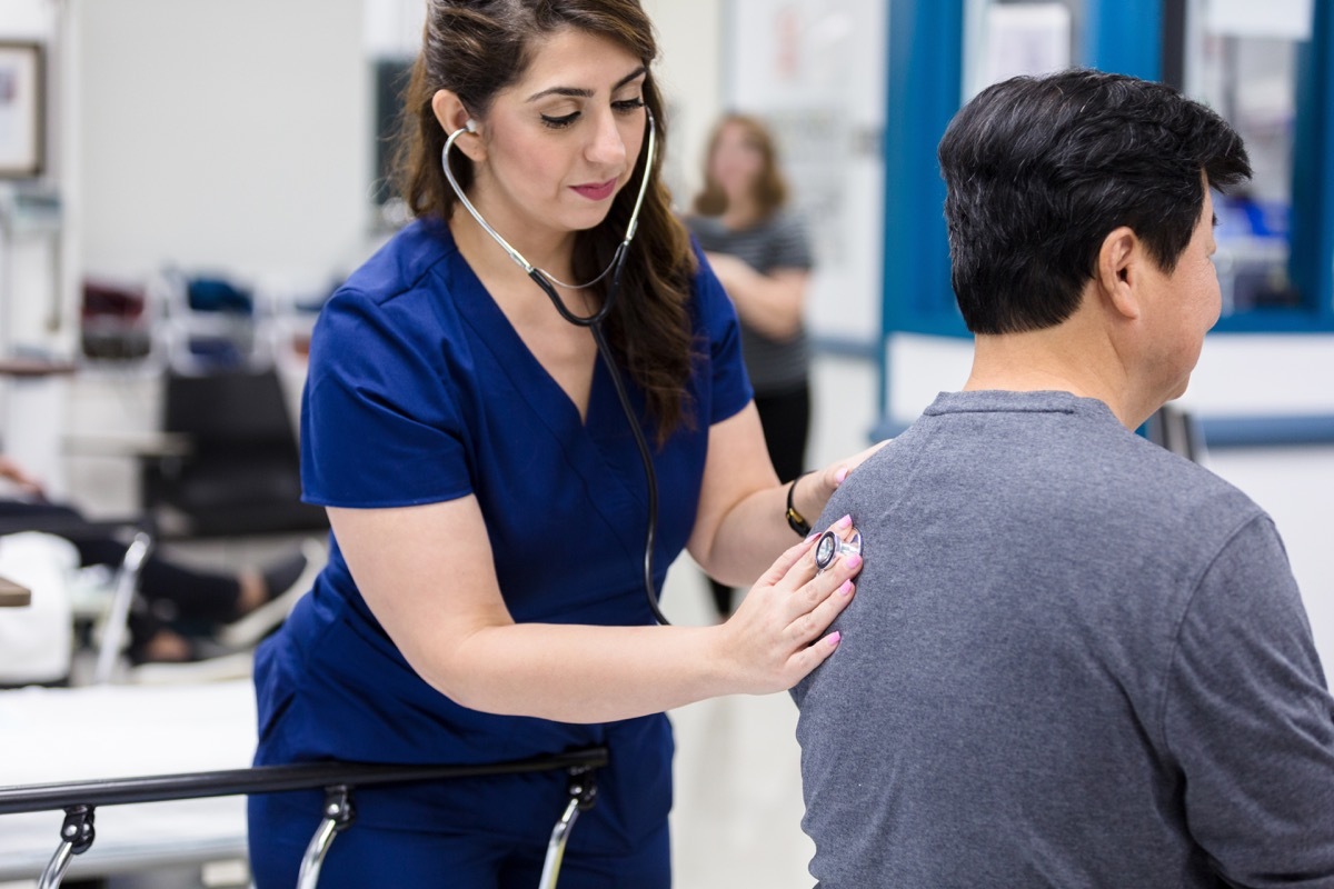 Caring ER doctor uses a stethoscope to listen to a senior male patient's lungs.