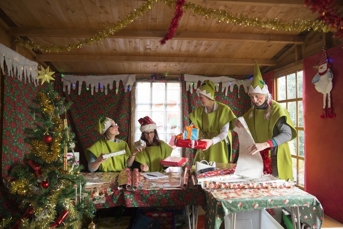 Four women dressed as Santa's elves wrap presents for Christmas.