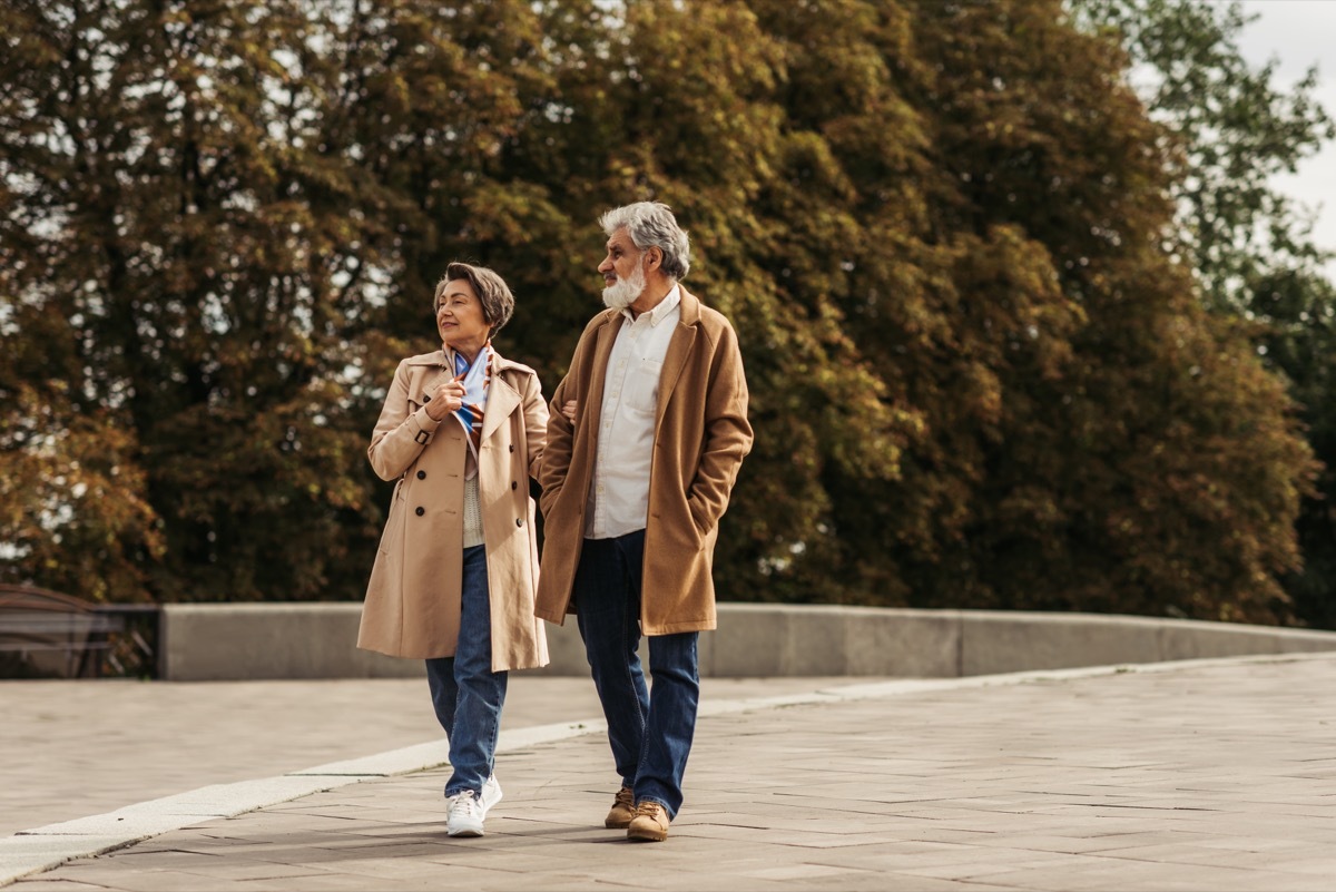 full length of smiling senior woman and bearded man in coat walking outside