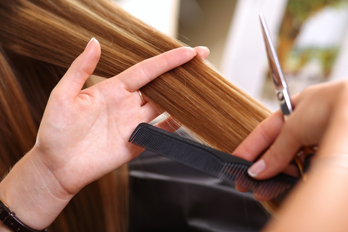 Female hairdresser hold in hand between fingers lock of hair, comb and golden scissors closeup. Hairdresser salon, barber shop, perfect look, new hairdo and color, straightening concept