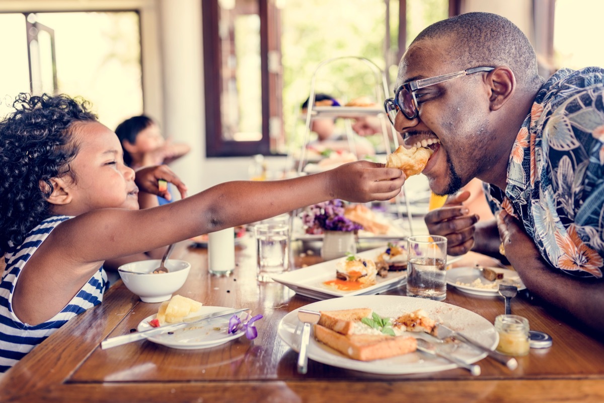 Child feeding his dad at breakfast playful