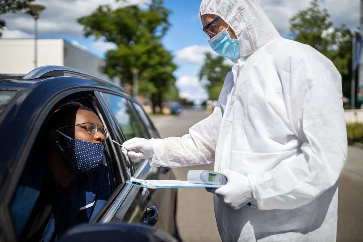 Doctor in a protective suit taking a nasal swab from a person to test for possible corona virus infection on the street. Diver through covid-19 testing center in city.