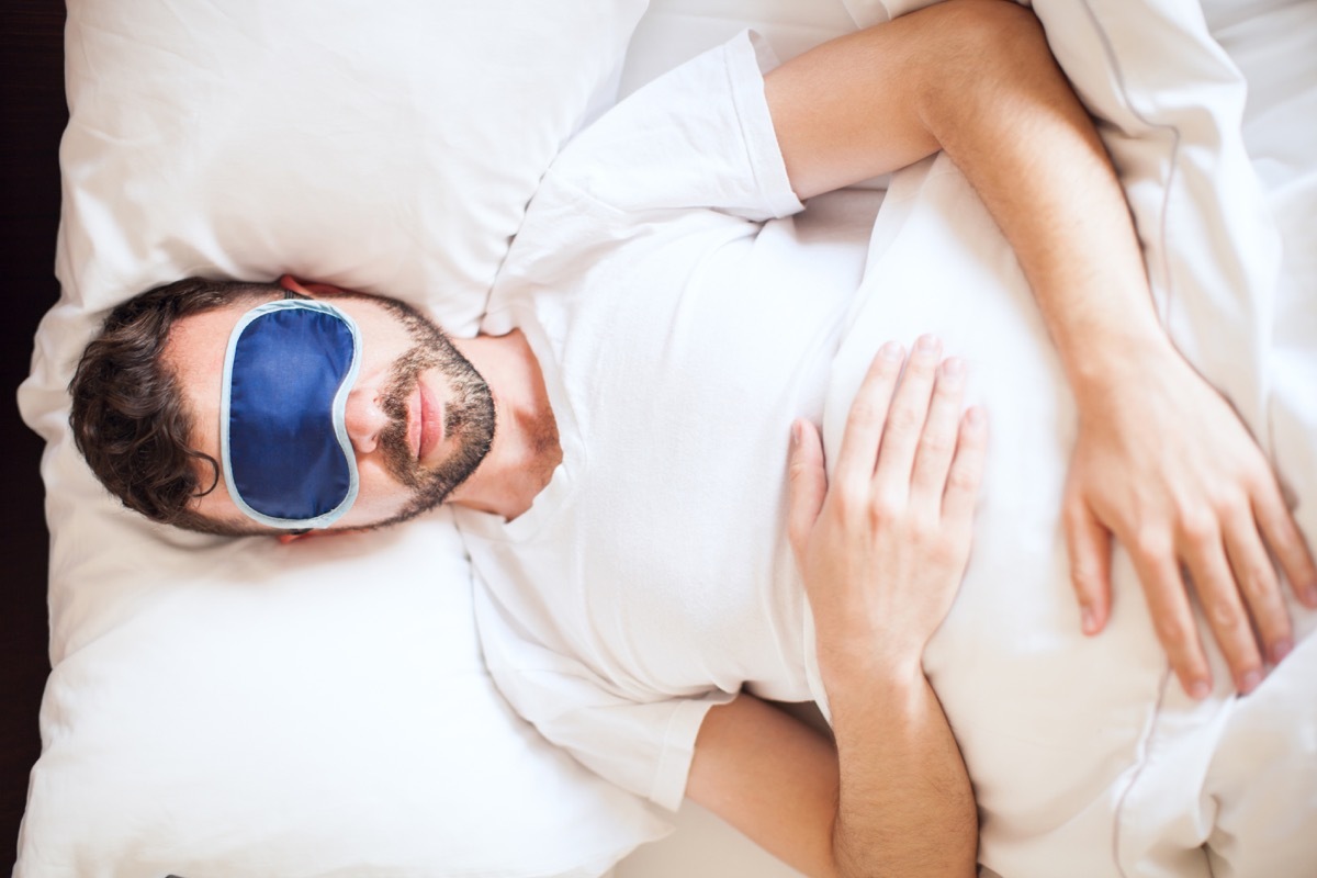 Top view of a young man wearing a sleep mask while getting some rest in his bedroom