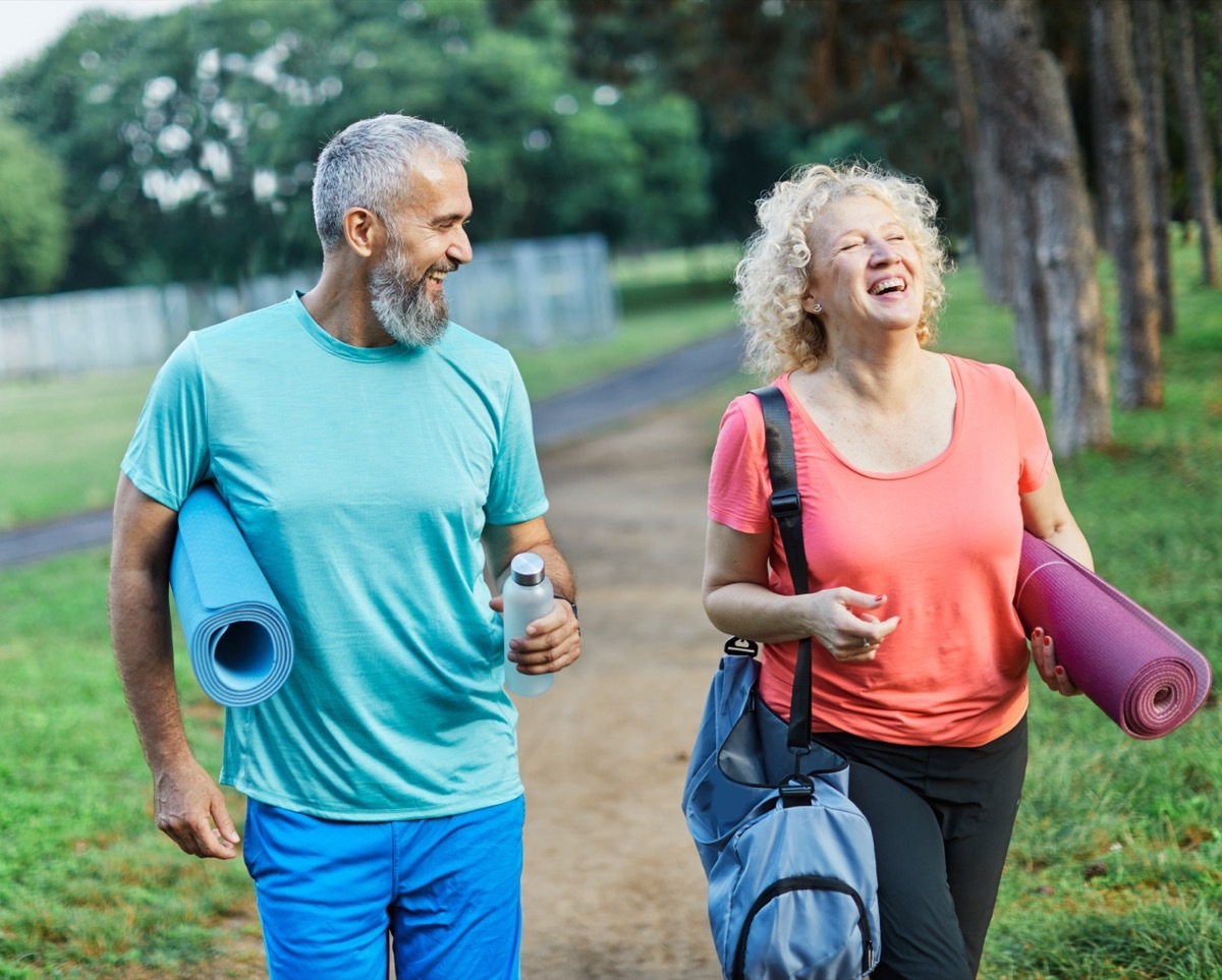 man and woman walking through park holding yoga mats and laughing