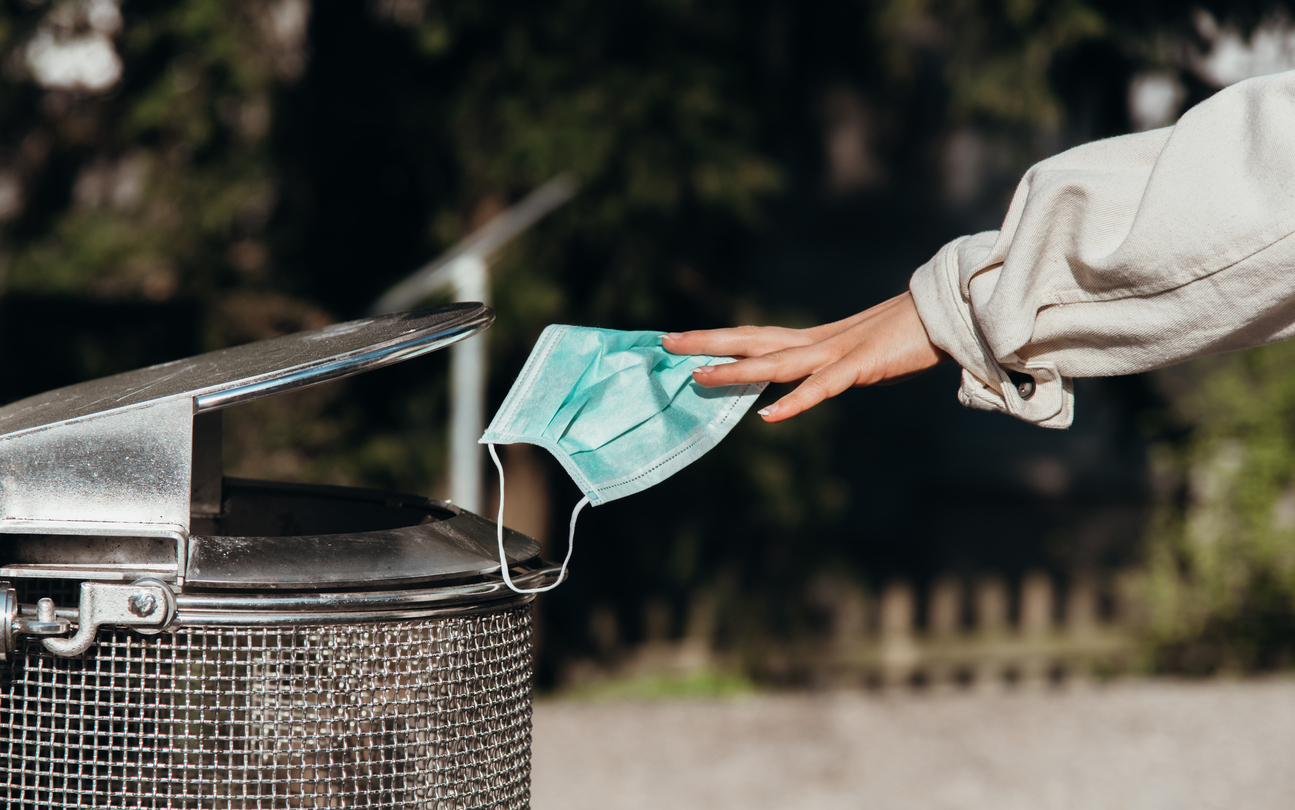 A person throwing away a face mask into a garbage can.