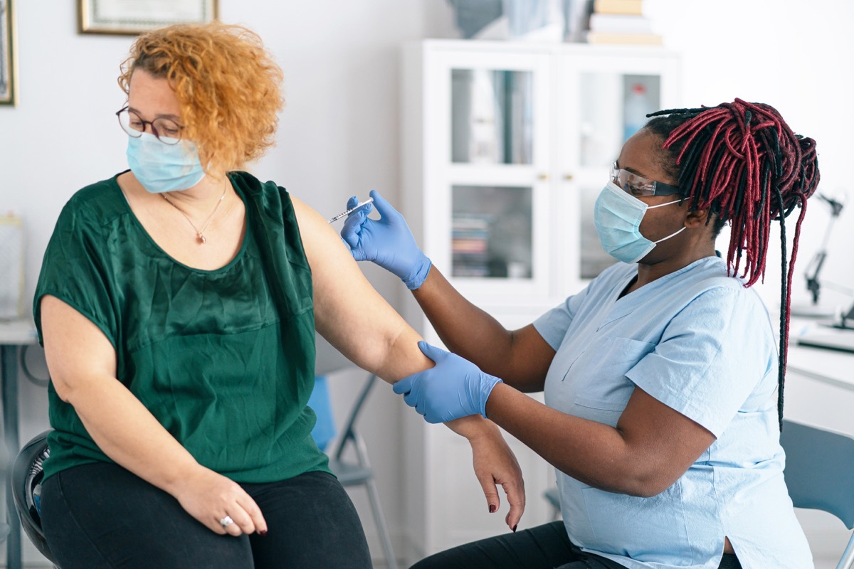 female doctor giving COVID-19 vaccine of a mid adult women with protective face mask in the doctor's office