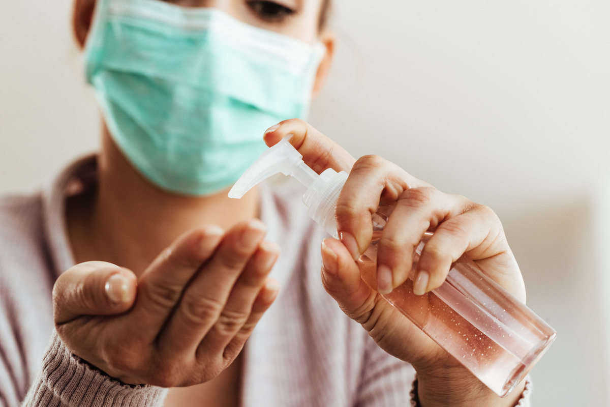 Close-up of woman wearing a mask using hand sanitizer at home.