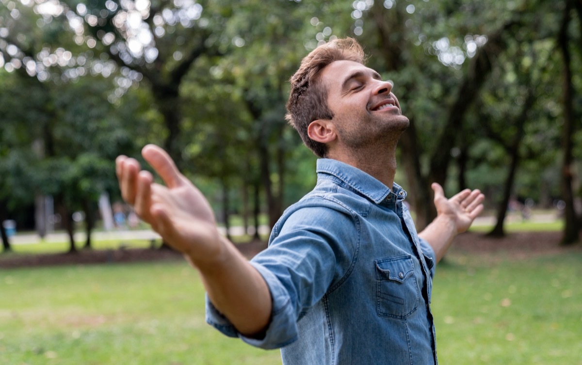 white man closing his eyes and putting his arms out to relax in the park