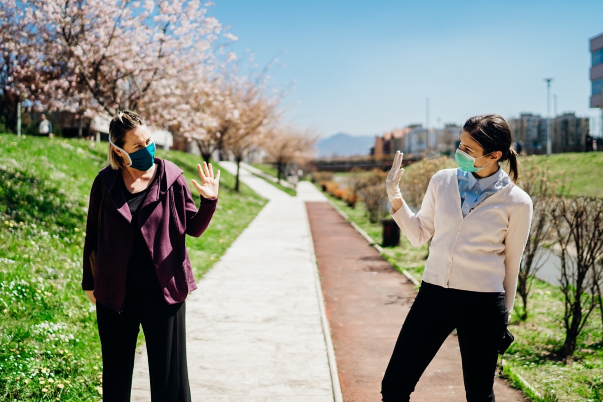 Two friends with protective masks greet with waving to each other.Alternative greeting during quarantine to avoid physical contact