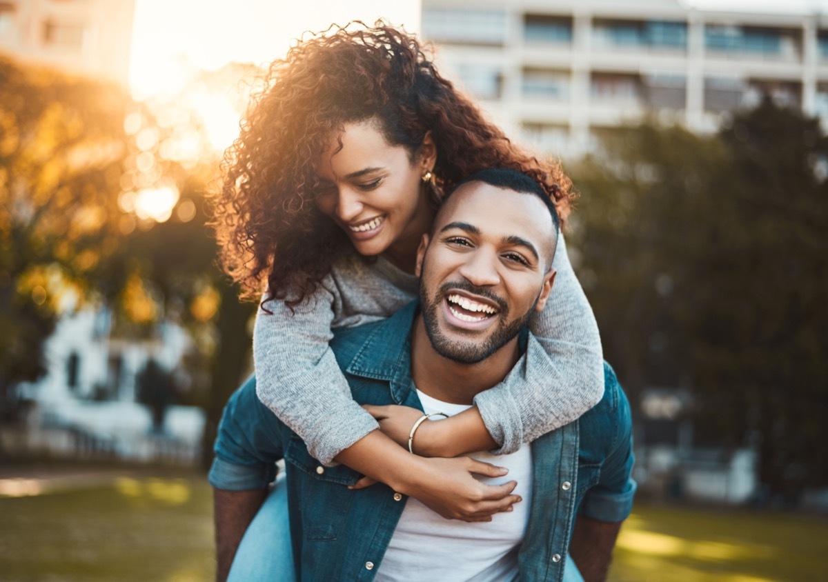 smiling man giving his girlfriend a piggyback ride