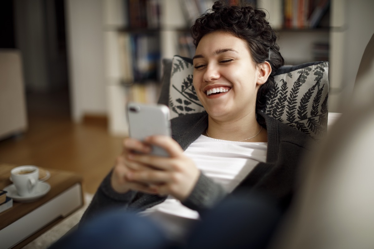 Young woman enjoying a relaxing weekend at home laughing while on phone