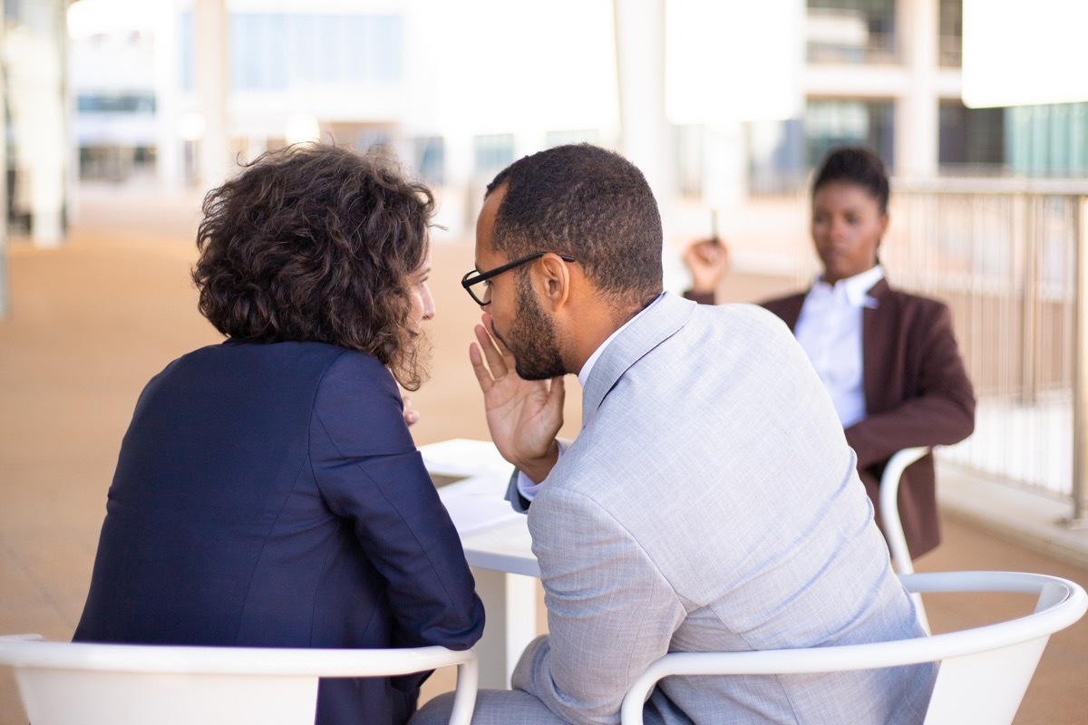 employees gossiping about young female colleague by whispering to each other