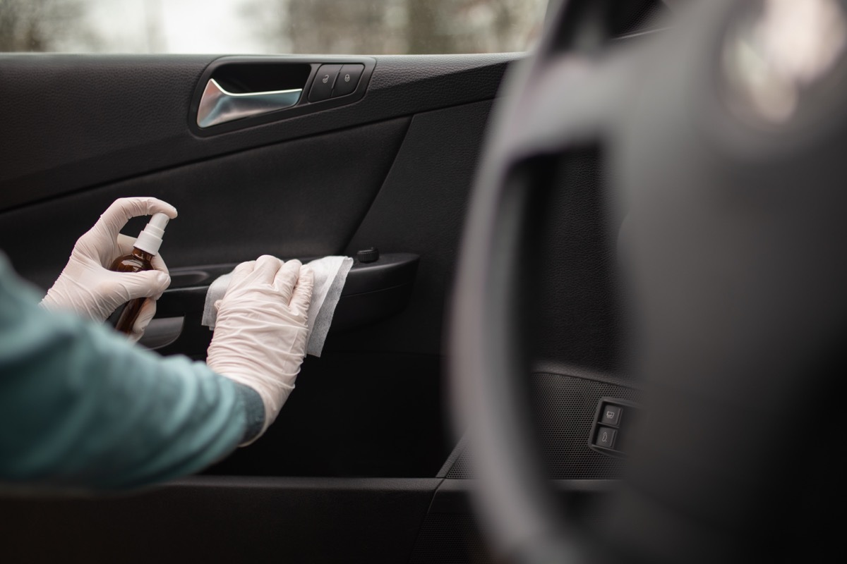 Person disinfecting and cleaning car interior with antiseptic liquid and wet disinfection wipes. Door handle is one of dirtiest parts in car and can contains viruses and bacteria.