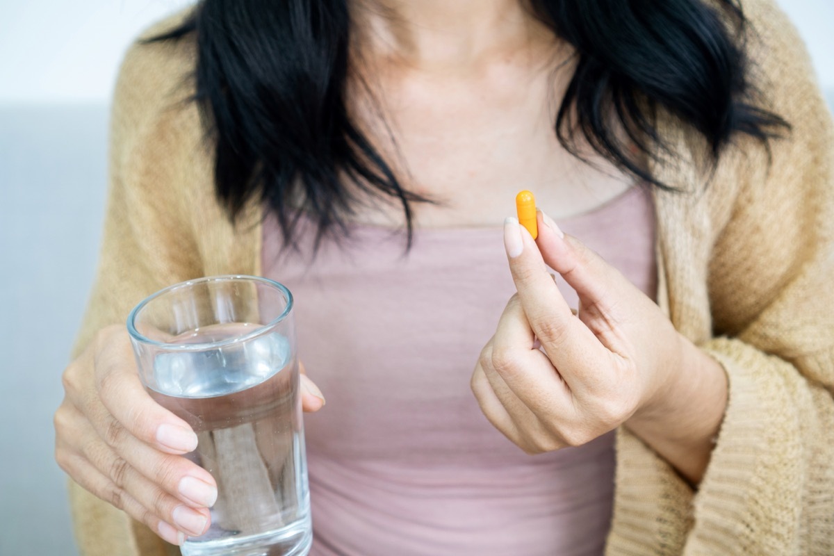 Closeup of a woman holding a turmeric supplement in one hand and a glass of water in the other