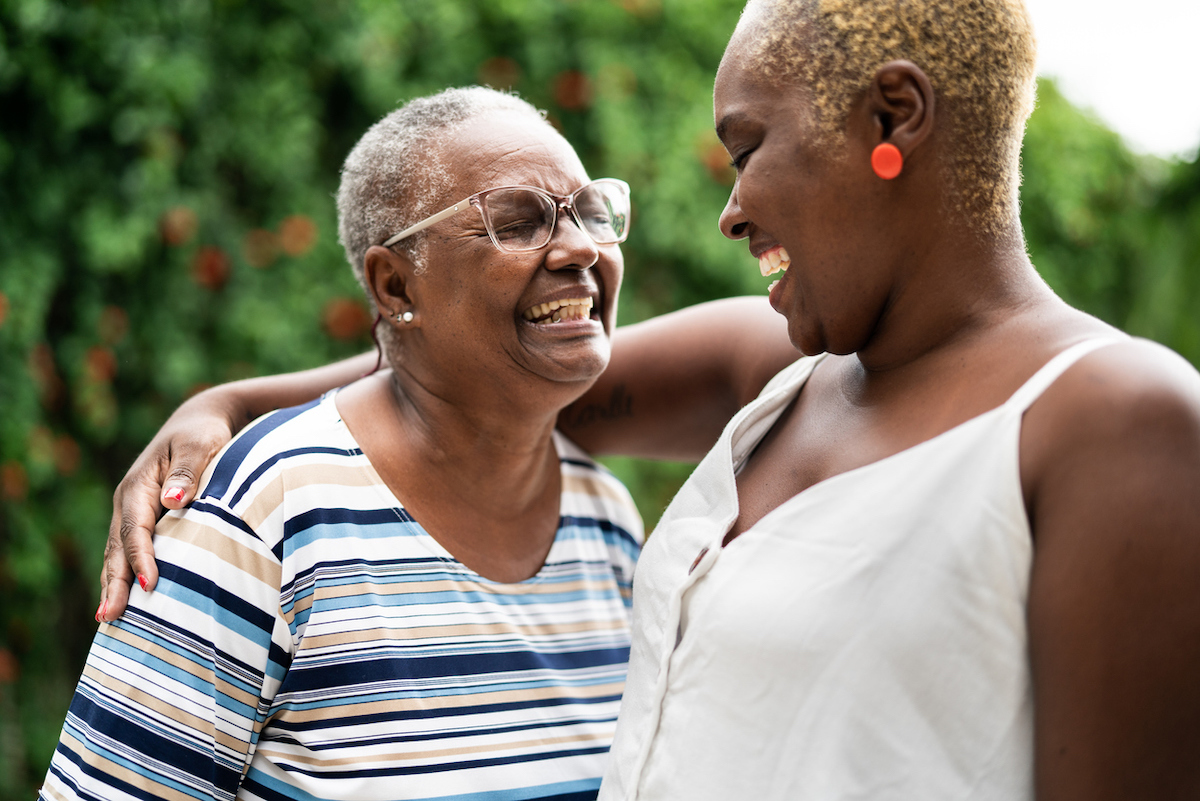 Mother and daughter embracing and smiling at each other outside.