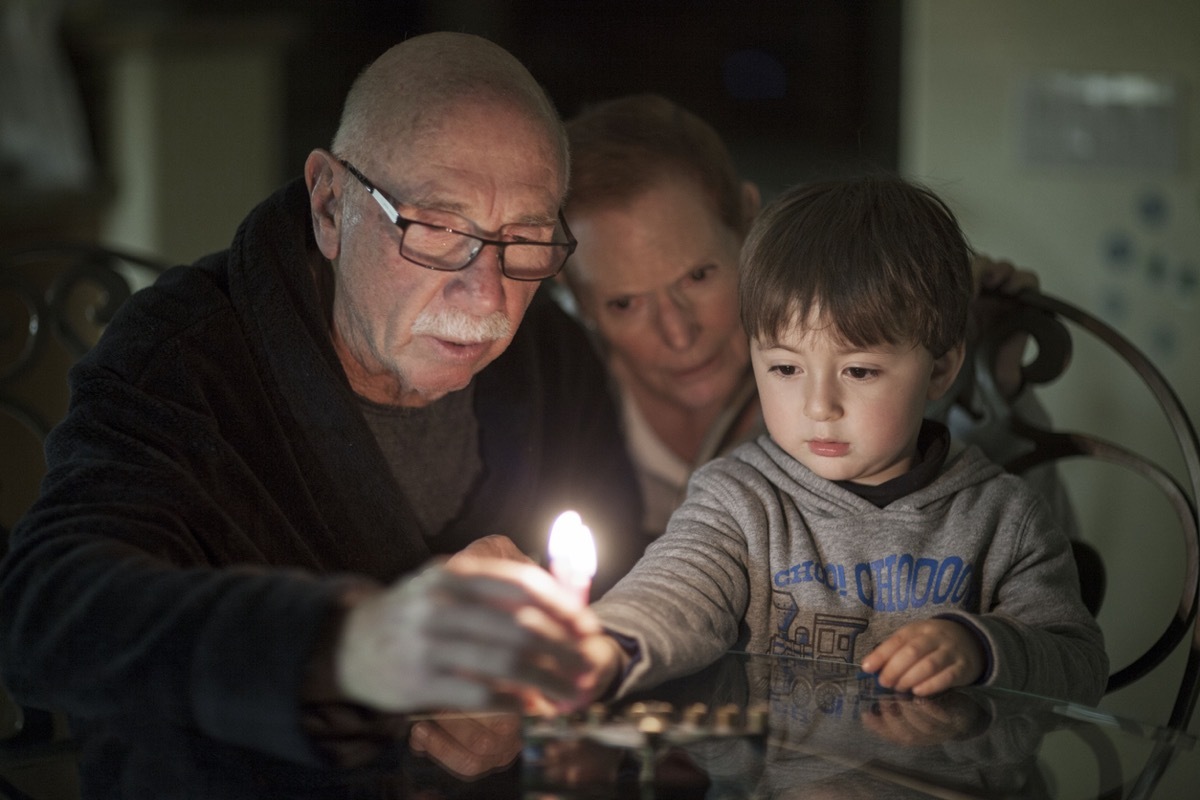 young white boy and grandparents lighting menorah