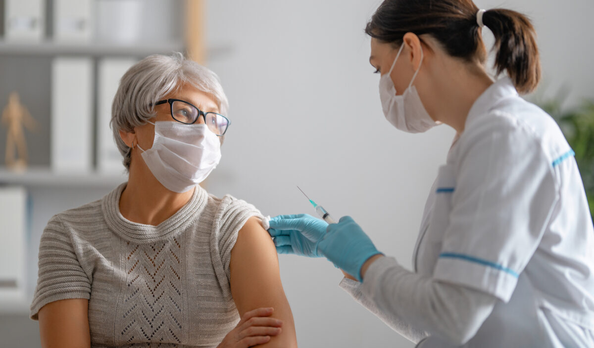 A senior woman wearing a face mask receives a COVID-19 vaccine from a female doctor.