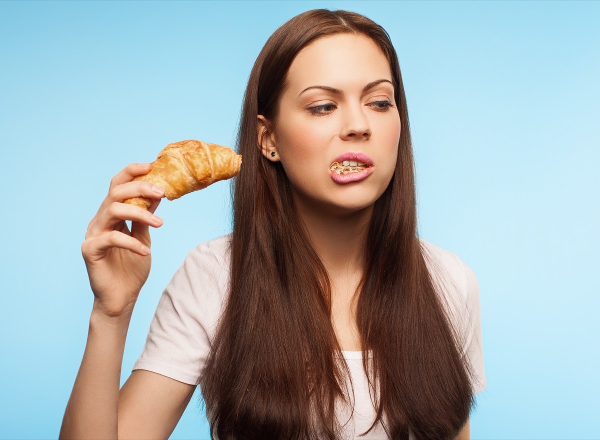 Woman eating croissant with open mouth.