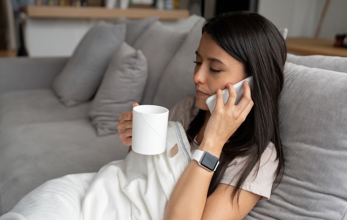 Sick woman with the flue in quarantine at home drinking tea and talking on the phone - COVID concepts