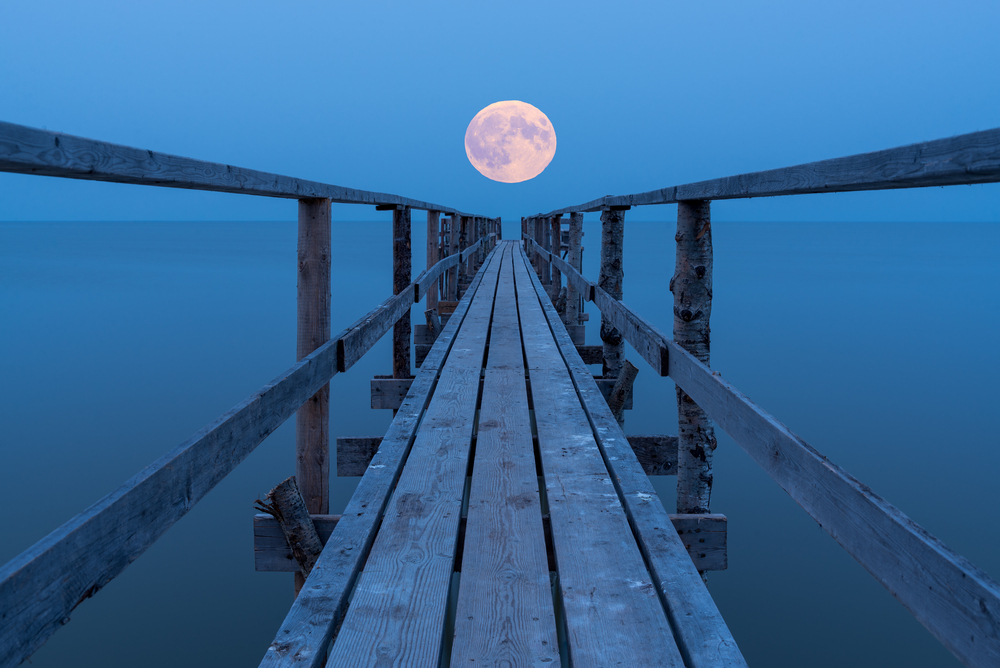 A full moon rising over a lake with a view down a long dock