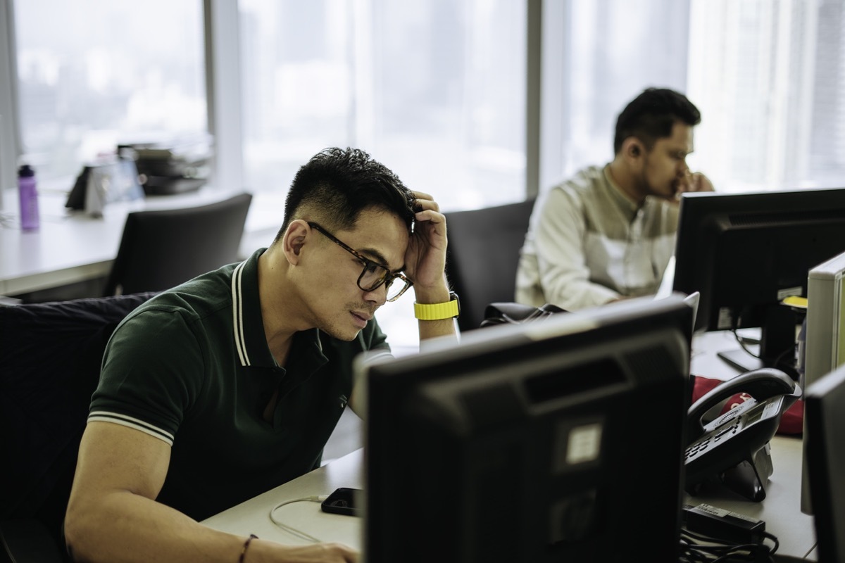 Shot of a young business man frowning while using a laptop in a modern officee