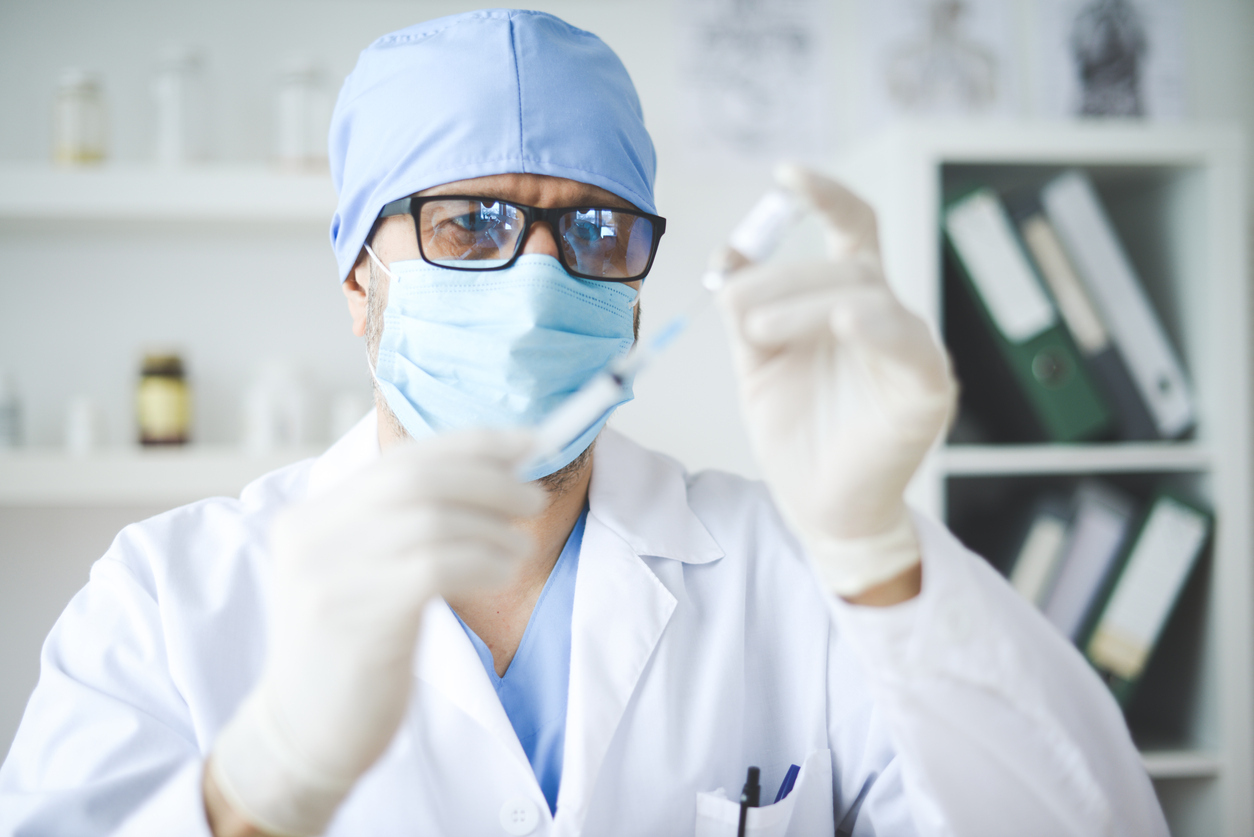 A healthcare worker wearing a face mask fills a syringe with a COVID-19 vaccine dose