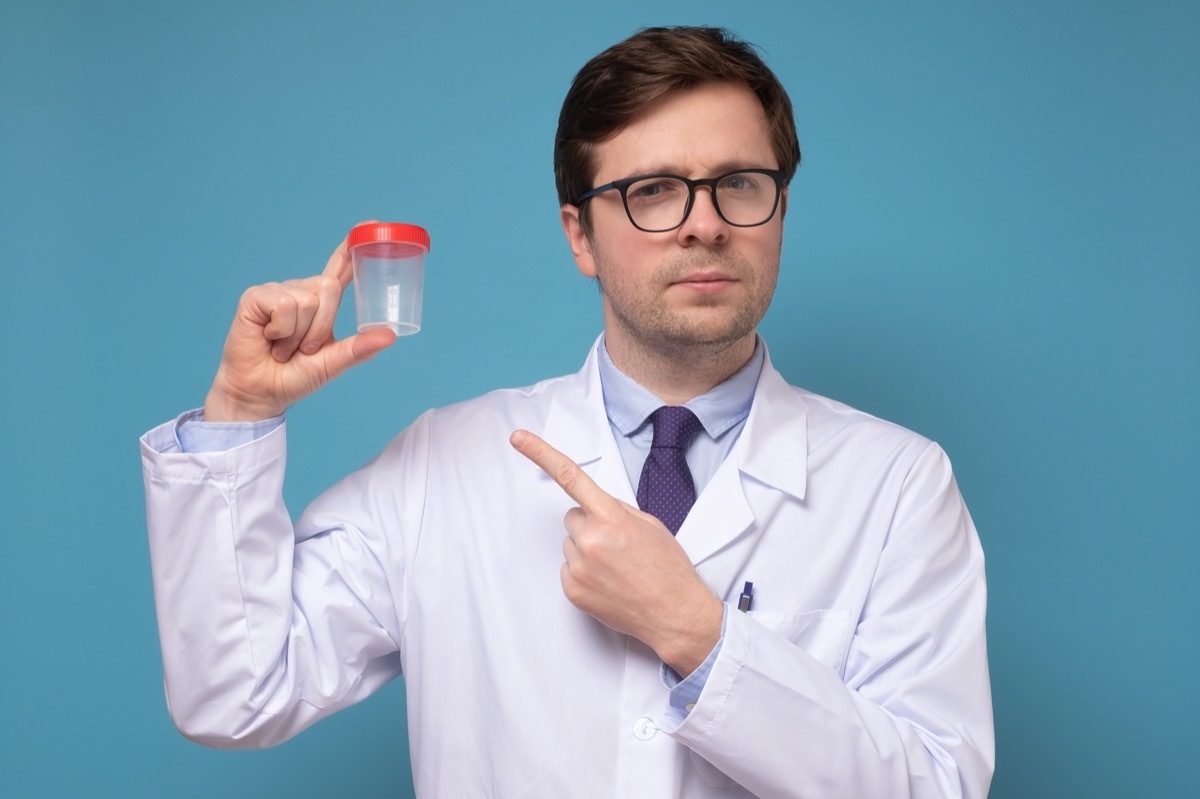 Mature caucaisan doctor or lab scientist holding urine sample cup