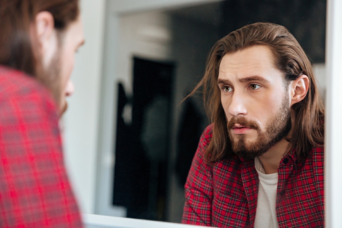 young bearded white man looking seriously in the bathroom mirror