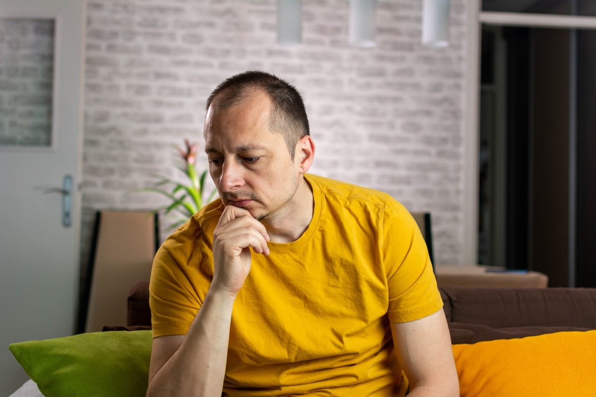 man sitting, yellow shirt, unhappy