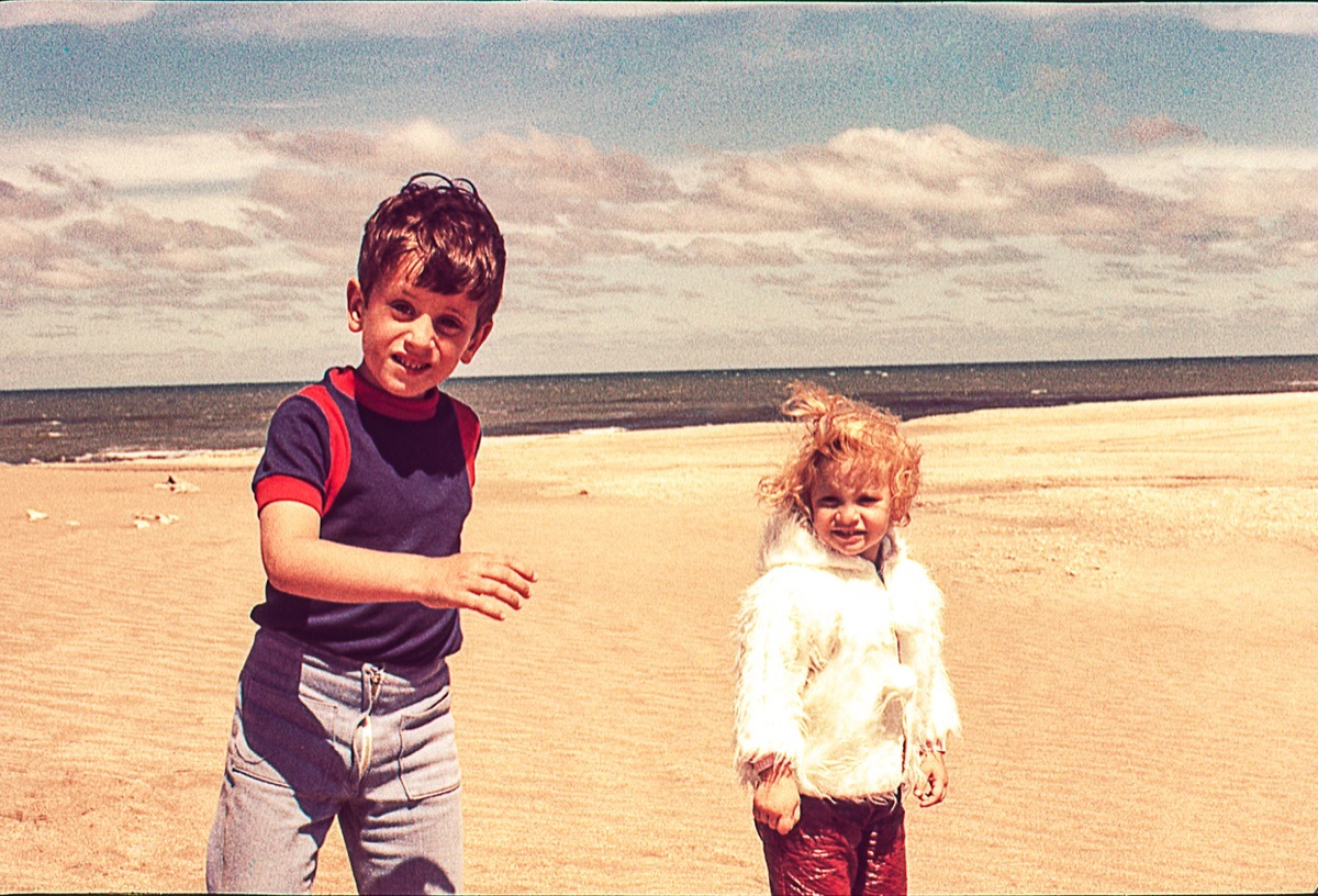 Vintage photo of a cute blonde little girl in with her brother at the beach on a cold day.