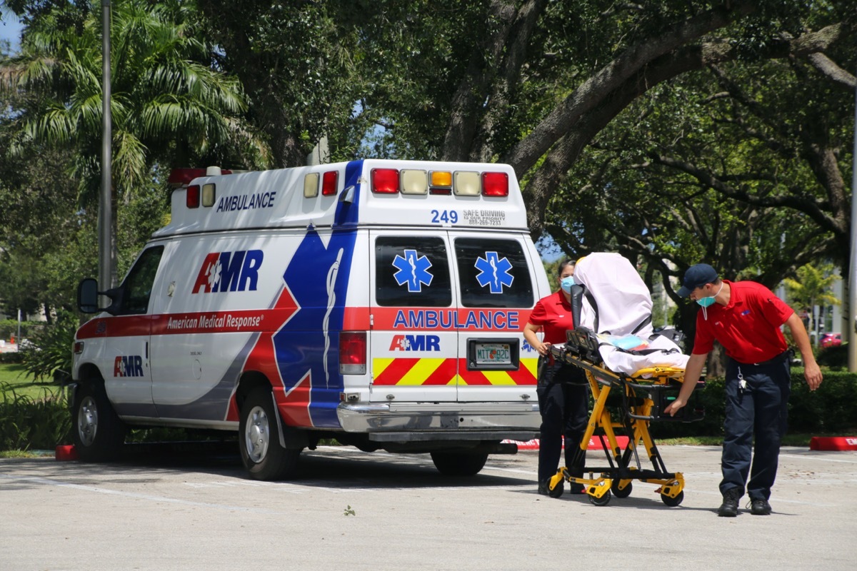 Male and female EMTs wearing face masks during Coronavirus pandemic remove gurney from ambulance parked at Boca Raton Community Hospital