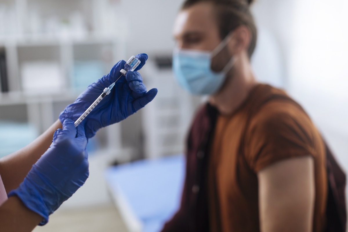 Young man waiting to get his vaccine by an unrecognizable nurse in the hospital