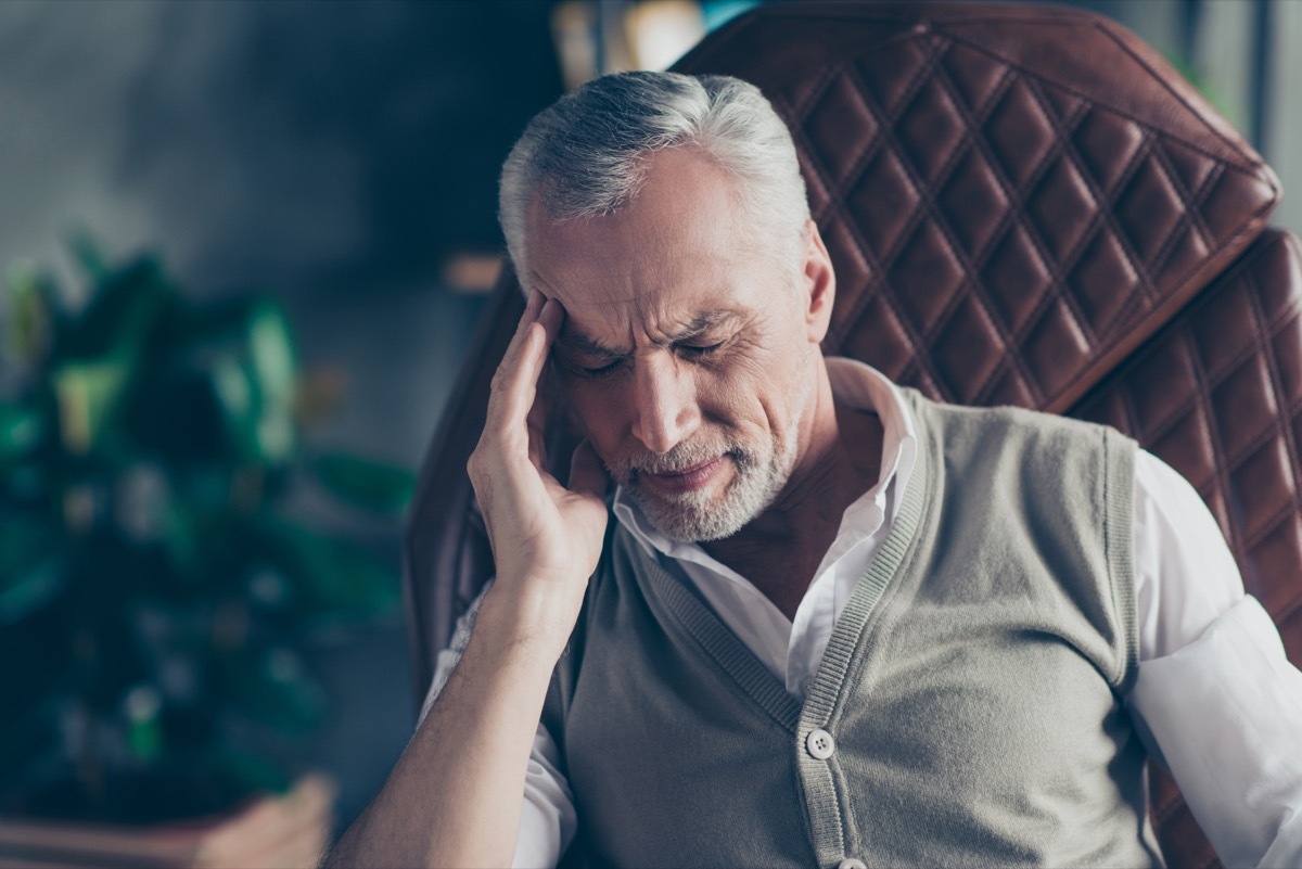 man sitting in an armchair suffering from a headache - what causes headaches