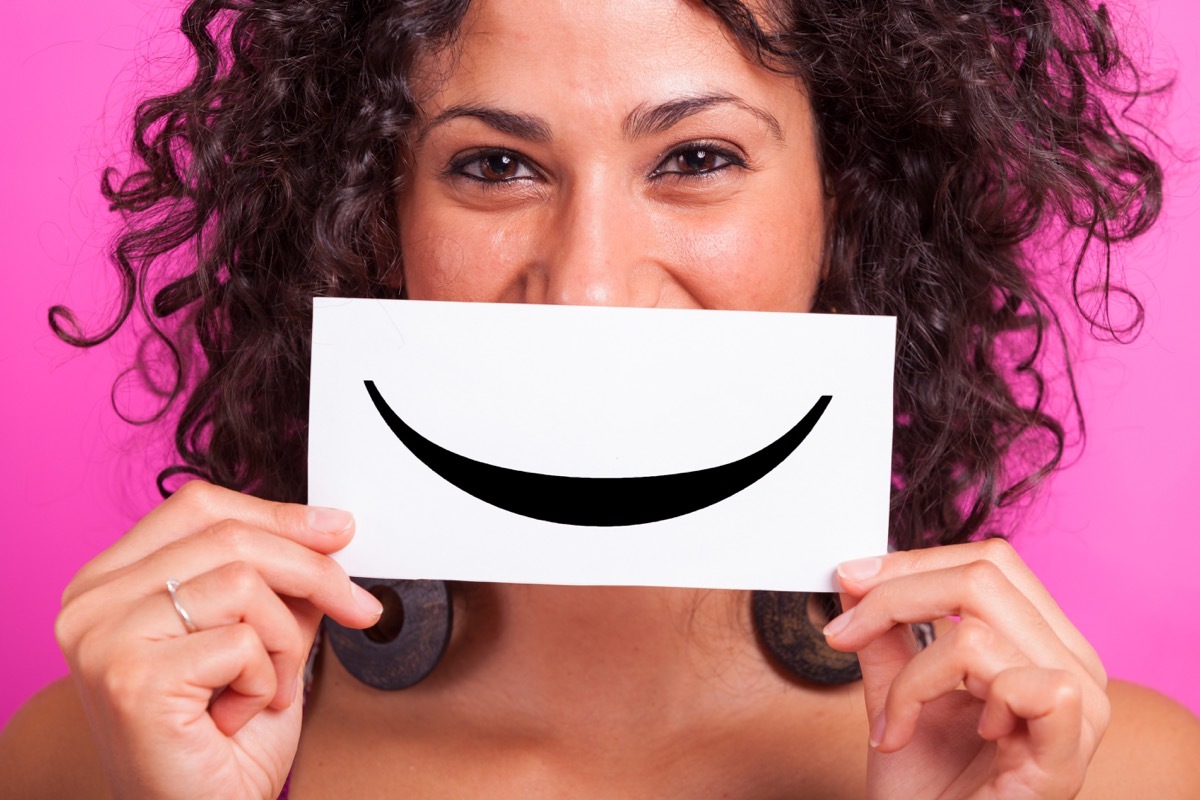 woman holding a smile face against a pink background