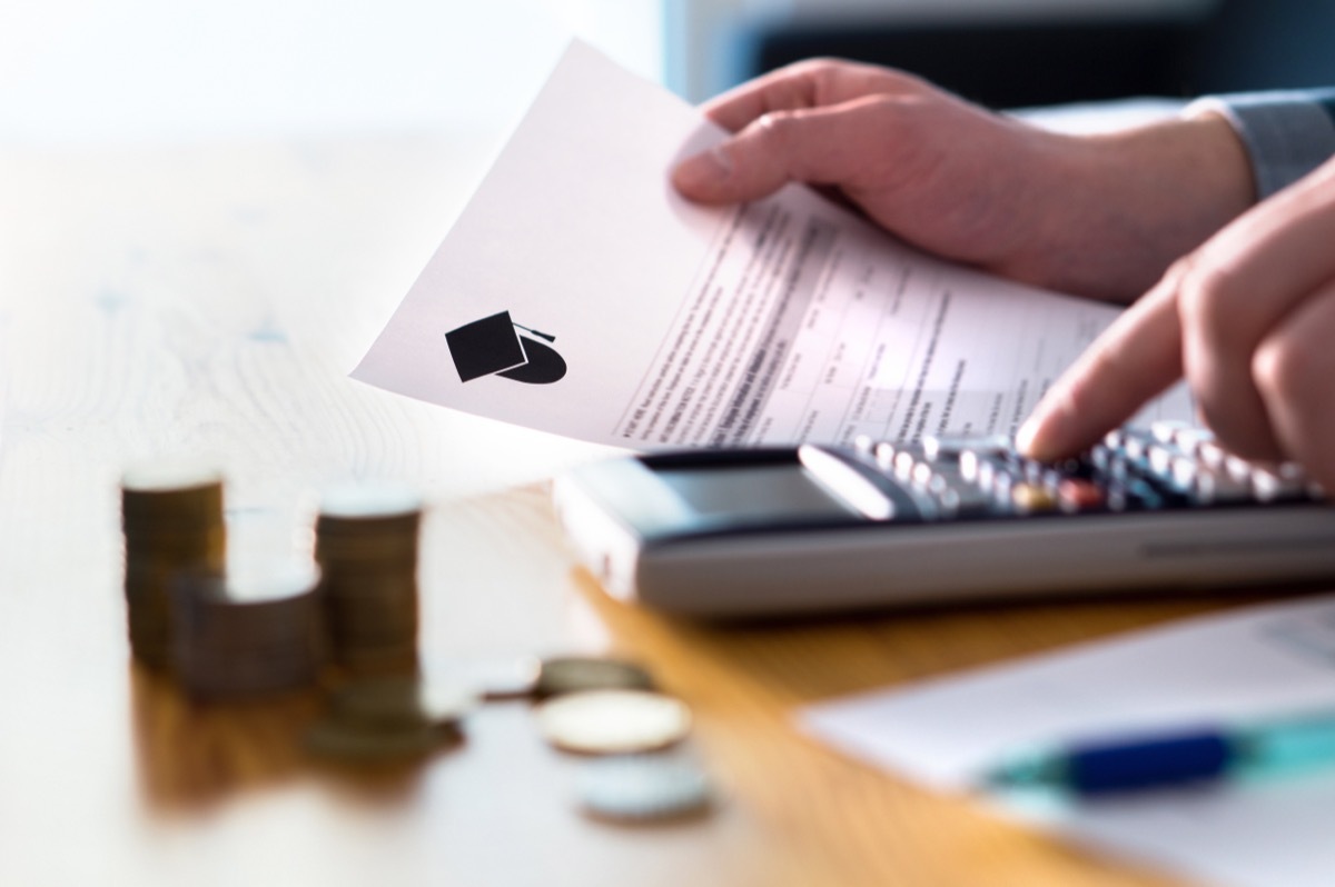 Man counting college savings fund, tuition fee or student loan with calculator. Education price and expenses concept. Money and papers on table. Calculating budget and planning finance.