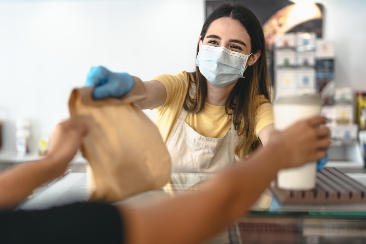 Bar owner working only with take away orders during corona virus outbreak - Young woman worker wearing face surgical mask giving takeout meal to customers - Healthcare and Food drink concept