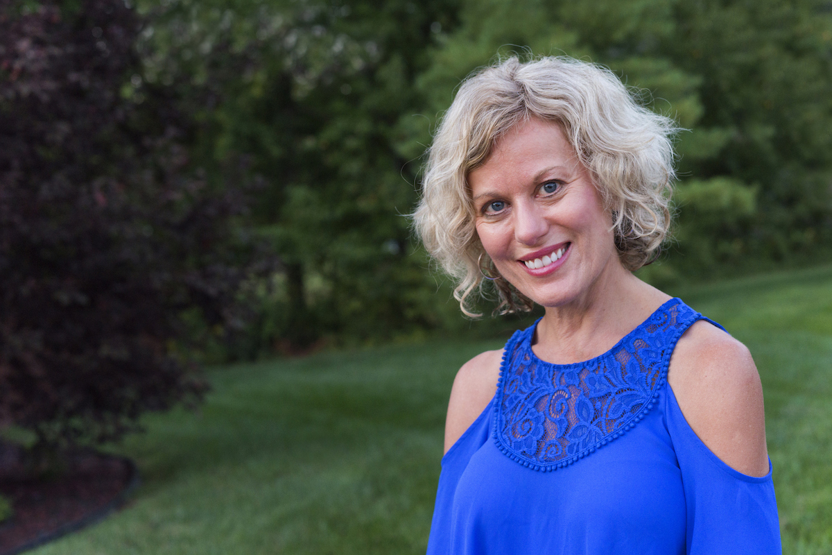 Smiling blonde woman wearing cobalt blue shirt in her 50's outdoors on a summer day