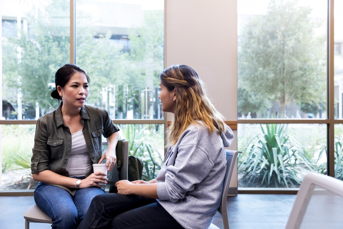 At the weekly veteran support group meeting, two female veterans sit apart from the group and share their stories with each other.