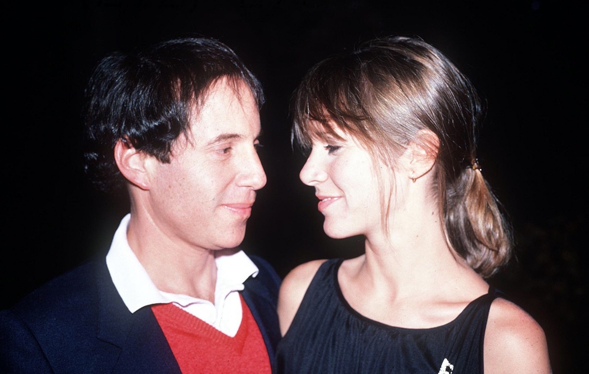 Carrier Fisher wears a black dress and Paul Simon wears a red sweater and black jacket in 1982