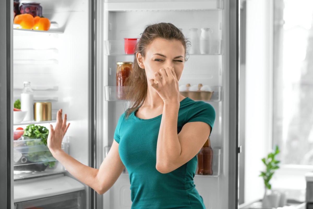 woman feeling bad smell from refrigerator in kitchen