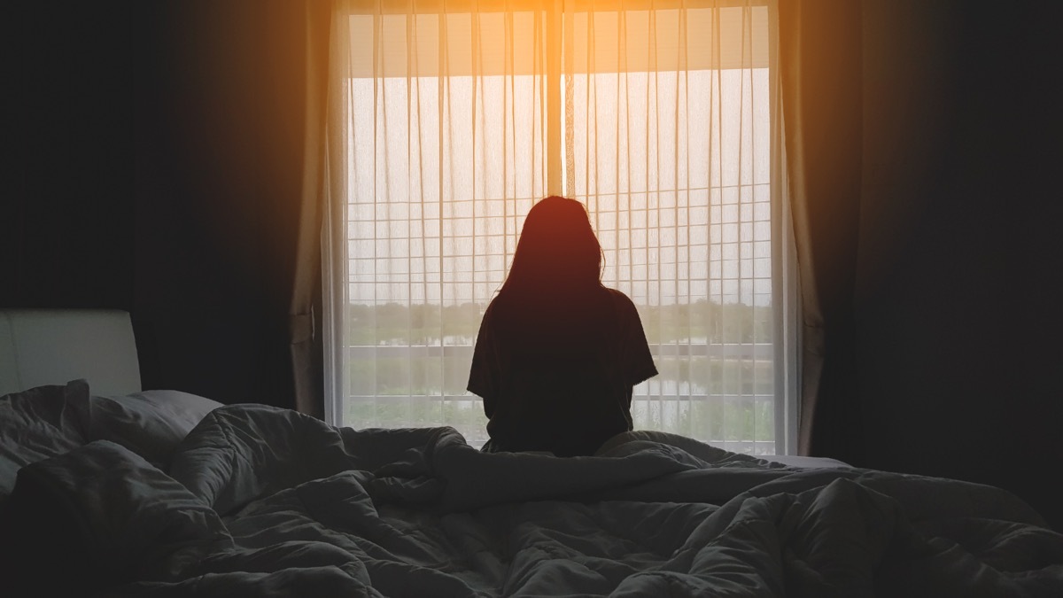 Woman alone in her bedroom looking out the window. 