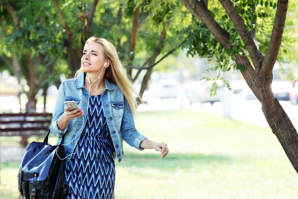 Young woman listening to music and walking in the park