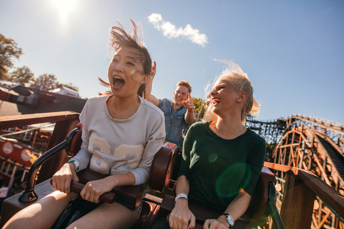 young people riding and screaming on a roller coaster at an amusement park