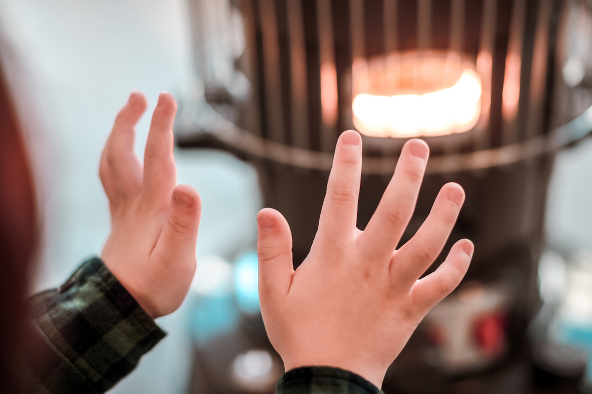 A young boy's hands warming up by heater